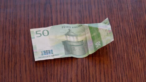 Hand-Placing-Norwegian-50-kr-Note-in-center-of-Wooden-Table