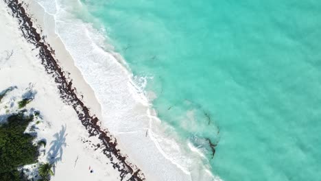 Aerial-hovering-above-the-mesmerizing-azure-and-turquoise-blue-waters-of-Isla-Blanca,-Mexico,-the-aerial-view-unveils-a-picturesque-scene-where-waves-gently-crash-onto-the-pristine-white-sand-beach