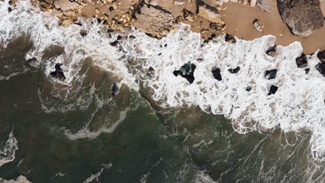 Aerial-top-down-shot-of-splashing-wavers-of-ocean-reaching-rocks-and-coast-of-Portugal
