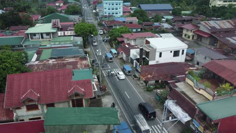 Drone-shot-of-small-Philippine-road-with-cars-passing-by,-surrounded-by-houses,-trees,-and-powerlines