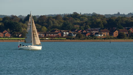 Kleines-Segelboot-Segelt-In-Solent-Southampton-In-Den-Rahmen-Hinein-Und-Aus-Ihm-Heraus,-Mit-Weston-Im-Hintergrund