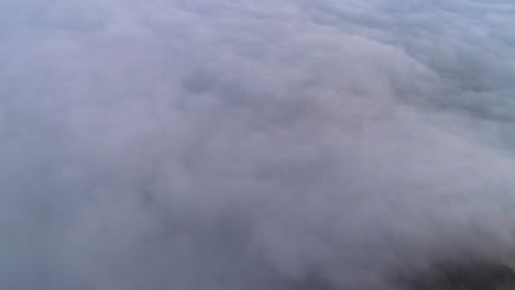 A-4K-drone-shot-above-low-lying-clouds,-flooding-over-mountain-tops-and-down-into-a-valley,-near-David-M