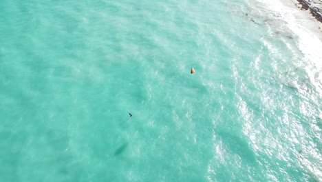 Aerial-captures-kite-boarder-gliding-over-sea-water-surface,-wind-power-with-a-power-kite-to-pull-a-rider-across-a-water,-location-Isla-Blanca,-Mexico
