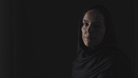 Eine-Muslimische-Frau-In-Düsterer-Stimmung-Wendet-Sich-Aus-Der-Dunkelheit-Ab-Und-Blickt-In-Die-Kamera