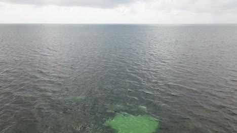 Drone-flight-over-the-green-ocean-water-on-a-cloudy-day