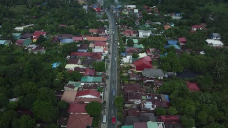 Drone-shot-of-Provincial-Philippine-Highway-Road,-with-cars-passing-by,-surrounded-by-trees-and-houses