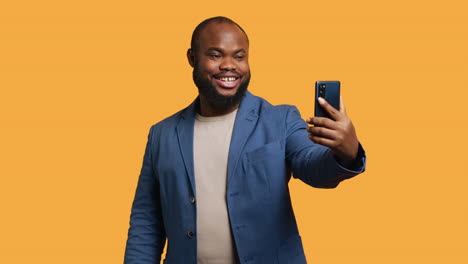 Joyous-man-using-smartphone-to-take-selfies,-studio-background