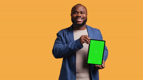 Amused-man-laughing-while-presenting-tablet-with-green-screen-display