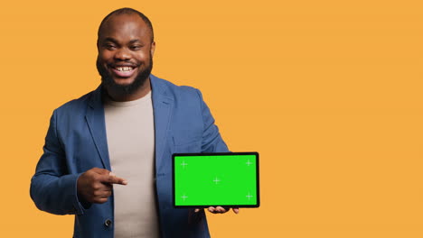 Upbeat-man-holding-green-screen-tablet,-doing-recommendation,-studio-background