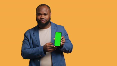 Man-showing-thumbs-down-sign-gesturing-holding-green-screen-phone