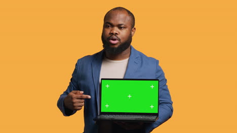 Jolly-man-holding-green-screen-laptop,-doing-recommendation,-studio-background