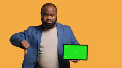 Man-showing-thumbs-down-sign-gesturing-holding-green-screen-tablet