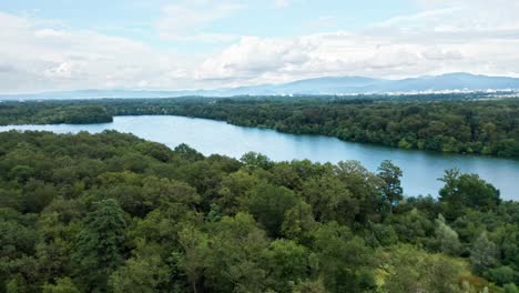 Lago-Azul-Entre-Los-Densos-Bosques-De-Un-Paisaje-De-Europa-Occidental-Bajo-Un-Cielo-Nublado,-Vista-Aérea-De-Drones