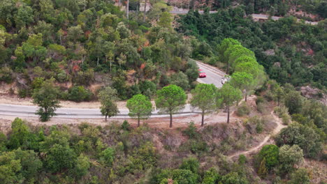 Drone-pan-shot-capturing-a-winding-road,-with-cars-gracefully-passing-through,-flanked-by-lush-green-trees-emerging-from-the-mountains