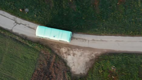 Turquoise-vanbus-driving-on-a-road,-drone-top-view