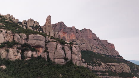 Drone-crane-down-shot-gracefully-revealing-the-round-cliff-peaks-of-Montserrat-against-the-backdrop-of-a-tranquil-overcast-day