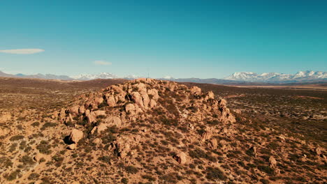 Dron-Dando-Vueltas-Alrededor-De-Una-Pequeña-Montaña-Coronada-Con-Una-Cruz,-Dejando-Ver-El-Pueblo-De-Malargüe-Y-La-Cordillera-De-Los-Andes-Al-Fondo