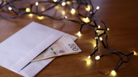 Polish-zloty-cash-in-an-envelope-as-a-Christmas-gift,-lying-next-to-the-Christmas-lights-on-the-table