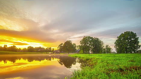 A-Time-Lapse-Shot-Of-A-Colourful-Sunset-View-At-A-Cottage-By-The-Lake-And-A-Green-Landscape