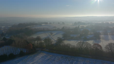 Establishing-Aerial-Drone-Shot-Over-Fields-and-Trees-in-Winter-on-Frosty-Snowy-Morning-in-UK