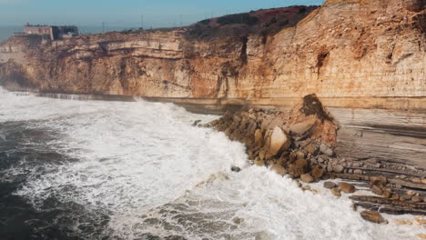 View-of-rocky-beach-with-crashing-waves-in-Nazare,-Portugal