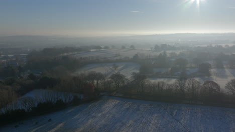 Establishing-Aerial-Drone-Shot-Over-Fields-and-Trees-in-Winter-on-Frosty-Morning-at-Sunrise-in-UK