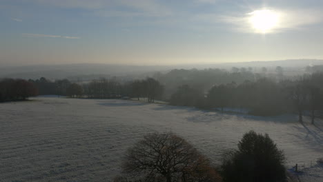 Aufsteigende-Luftdrohnenaufnahme-über-Feldern-Und-Bäumen-Im-Winter-An-Einem-Frostigen,-Nebligen-Morgen-In-Großbritannien