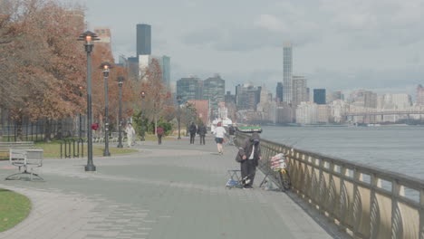 Autumnal-Scene-On-East-River-Waterfront-With-People-Walking,-Running-And-Fishing-In-New-York