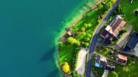 Aerial-view-over-buildings,-a-road-and-fall-colors-on-the-coast-of-lake-Attersee,-Austria