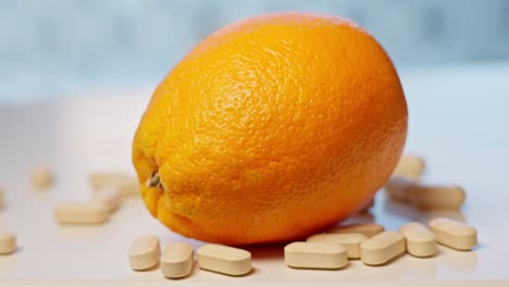 Vitamin-C-tablets-dropping-on-white-surface-beside-orange,-slow-motion-with-motion-blur