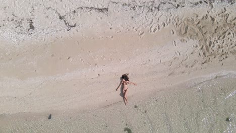 Ein-Sexy-Mädchen-Mit-Langen-Schwarzen-Haaren-Entspannt-Am-Strand,-Stellt-Einen-Braunen-Bikini-Zur-Schau-Und-Genießt-Eine-Sonnenverwöhnte-Bräune