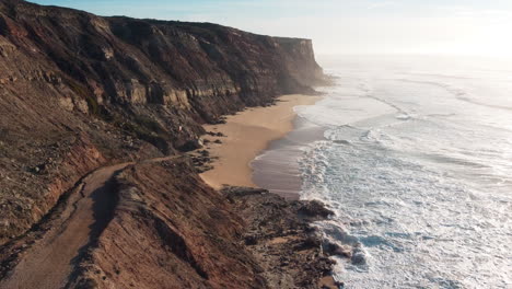 Filmischer-Drohnenflug-Entlang-Der-Küste-Portugals-Mit-Felsigen-Klippen-Und-Schäumenden-Meereswellen-Bei-Sonnenuntergang