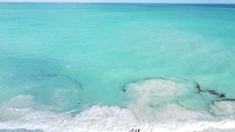 Ascending-aerial-footage-captures-people-in-the-shallow-waters-of-the-Caribbean-Sea-at-Isla-Blanca,-Mexico
