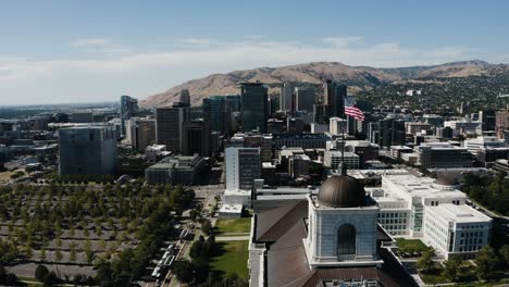 Drone-shot-pushing-past-the-American-flag-waving-over-downtown-Salt-Lake-City,-Utah