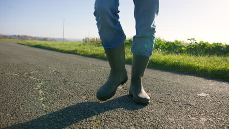 Wearing-jeans-while-walking-with-industrial-boots-on-asphalt-towards-the-grass-at-the-roadside,-low-angle-tracking-shot