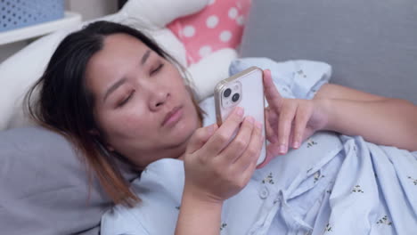 Lying-down-down-while-looking-at-her-phone's-screen,-a-woman-is-watching-some-videos-on-the-internet