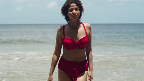 The-beauty-of-a-sunny-day-on-a-tropical-island-beach-is-captured-by-a-young-girl-with-curly-hair-in-a-striking-red-bikini-walking-on-the-beach