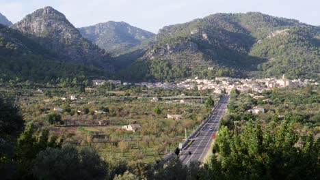 Amidst-a-serene-Mallorcan-autumn-evening,-a-single-car-traverses-the-picturesque-road-leading-to-Caimari,-nestled-amidst-lush-hills,-capturing-the-peaceful-essence-of-the-village