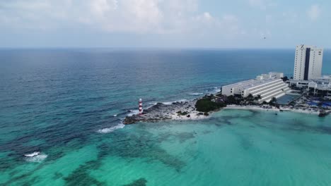Aerial-of-Punta-Cancun-Lighthouse,-an-iconic-landmark-in-Cancun,-Mexico,-surrounded-by-a-panoramic-view-of-the-turquoise-waters-of-the-Caribbean-Sea