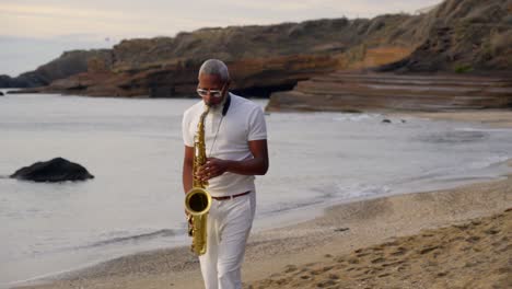 Langsame,-Aufschlussreiche-Aufnahme-Eines-Mannes,-Der-Bei-Sonnenuntergang-Am-Strand-Saxofon-Spielt