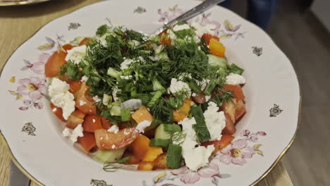 Up-close-Greek-salad-in-floral-plate,-cucumber,-tomato,-feta-cheese,-pepper