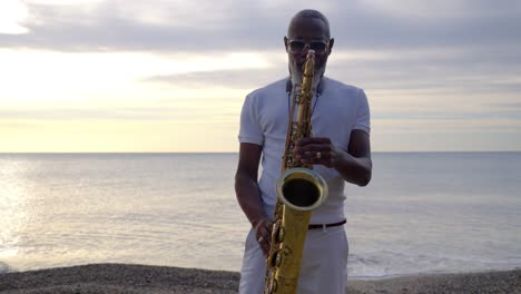 Saxophonist-plays-his-saxophone-on-the-beach-in-Sete,-France,-as-the-sun-sets-over-the-Mediterranean-Sea