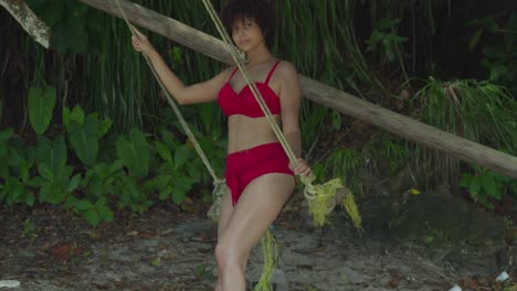 On-a-sunny-day,-a-tropical-island-becomes-the-setting-for-a-young-girl-in-a-red-bikini-with-curly-hair-on-a-swing