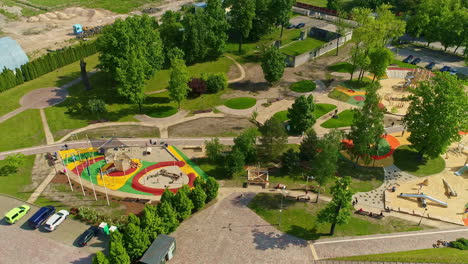 Aerial-drone-shot-flying-high-over-kids-playing-in-a-recently-constructed-kids-city-park-at-daytime