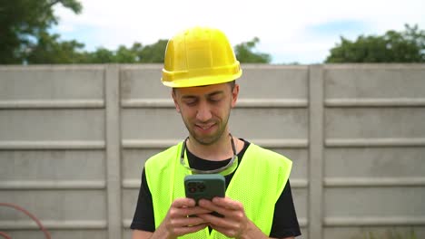 General-Labourer-In-Hard-Hat-And-Safety-Vest-Typing-On-Smartphone-Outdoor