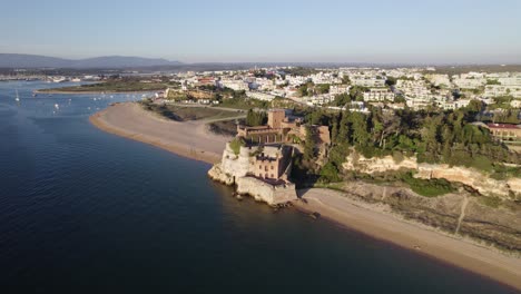 Hermoso-Castillo-Medieval-En-La-Playa-De-Arena-En-Ferragudo,-Portugal,-órbita-Aérea