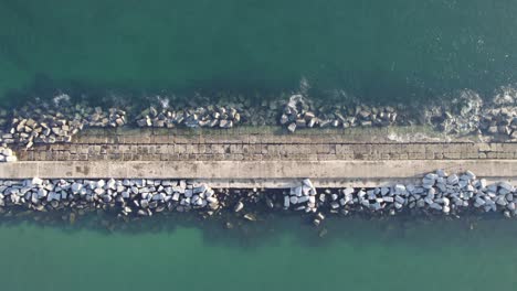 Aerial-top-down-slider-view-Pier-in-the-ocean-with-rocky-stones,-breakwater
