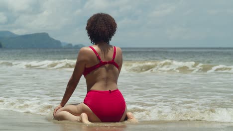 A-tropical-island-beach-comes-to-life-as-a-young-girl-with-curly-hair-kneel-in-the-sand-in-a-red-bikini-on-a-sunny-day