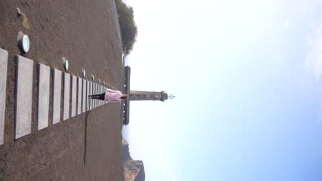 Frau-Geht-Auf-Vulkanasche-Mit-Dem-Leuchtturm-Ponta-Dos-Capelinhos-Im-Hintergrund,-Faial,-Azoren