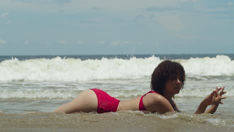 Ein-Junges-Mädchen-Im-Roten-Bikini-Mit-Lockigem-Haar-Erhellt-An-Einem-Sonnigen-Tag-Eine-Tropische-Insel-An-Der-Küste-Mit-Meereswellen-Im-Hintergrund